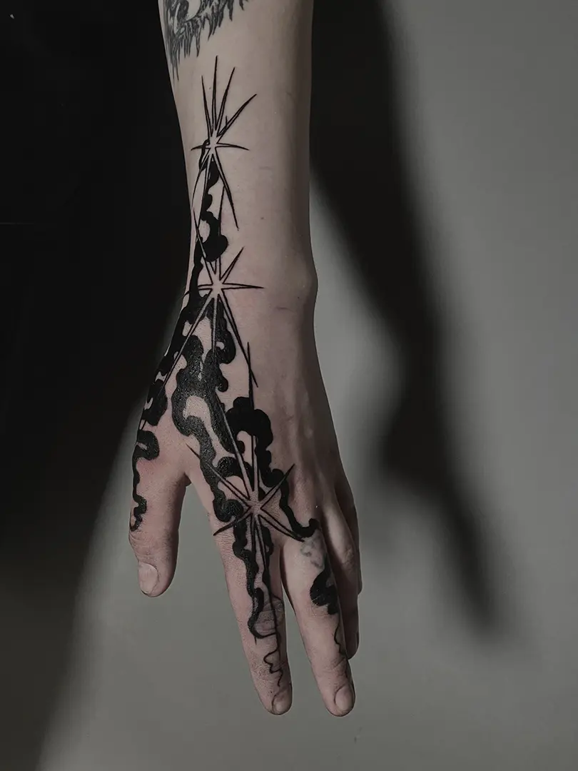 Tatuaje Abstracto con formas que juegan con el humo y las estrellas realizado en la zona lateral de la mano, incluyendo los dedos índice, corazón y pulgar. Está hecho en técnica Blackwork por la tatuadora Marta Tanta, en Bilbao