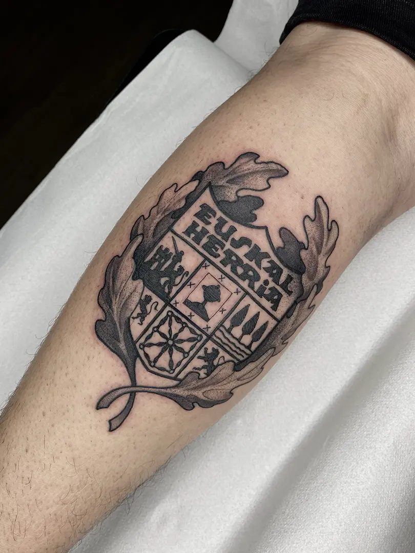Tatuaje realizado en técnica blackwork del escudo de Euskal Herria con unas hojas de roble alrededor. Hecho en el gemelo, por Moi en el estudio Karratu Tattoo