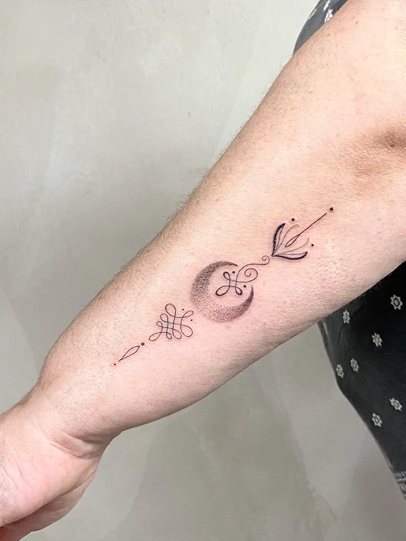 tatuaje de un unalome de línea fina con más símbolos ornamentales y una luna realizada en dotwork en el brazo por Tikka Tattoo en Karratu Tattoo.