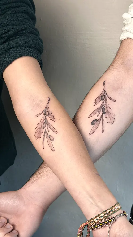 Tatuaje de amigos o familia de una rama de olivo realizada en línea fina con unas hojas de roble (Italia y País Vasco) hecho en blackwork con whip shading