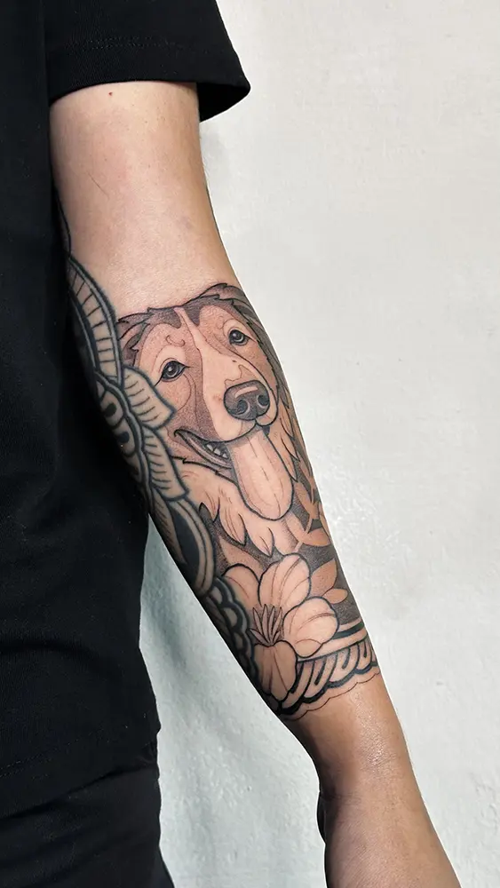 Tatuaje estilo Neotradicional de un perro, personalizado y adaptado al estilo ornamental del otro tatuaje añadiéndole motivos florales y ornamentales. El tatuaje tiene linea sólida y sombreados suaves en blanco y negro.