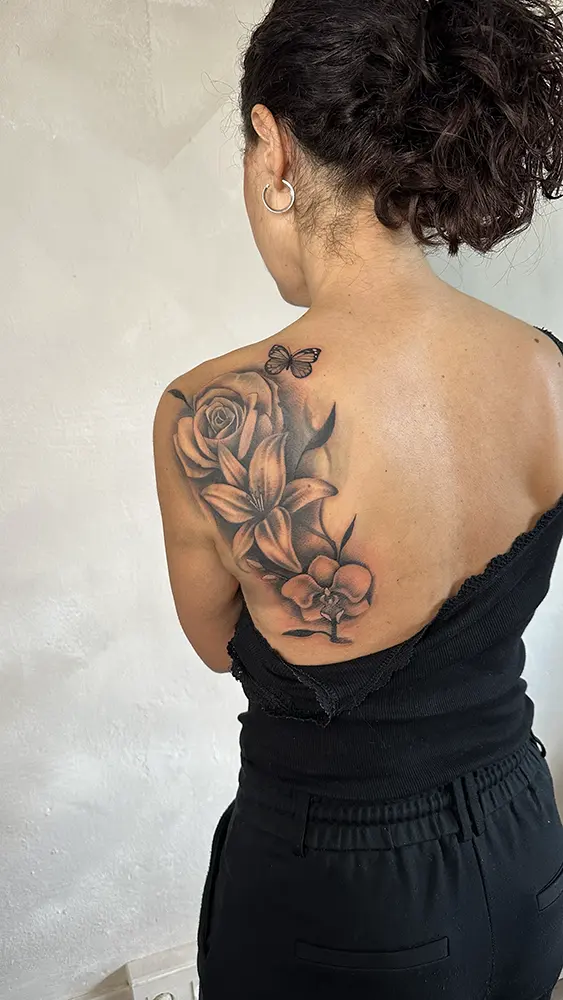 Tatuaje restaurado en la espalda, originalmente eran un lirio y una rosa y al que se le ha añadido una orquídea y una mariposa. Se le ha redefinido la forma añadiendo oscuridad y sombras