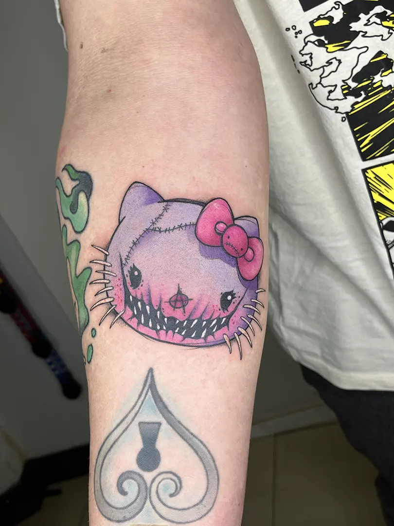 Tatuaje a color rosa y morado de Hello Kitty como si fuera una muñeca de trapo de estética dark, realizado por Don Ander en Bilbao