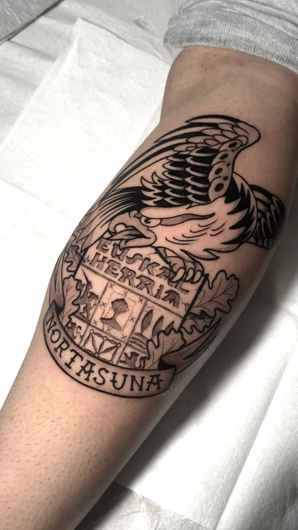 Tatuaje estilo tradi o tradicional con el estilo de euskal herria con estilo grabado. Tiene unas hojas de roble (aritz) alrededor y una banda que pone 