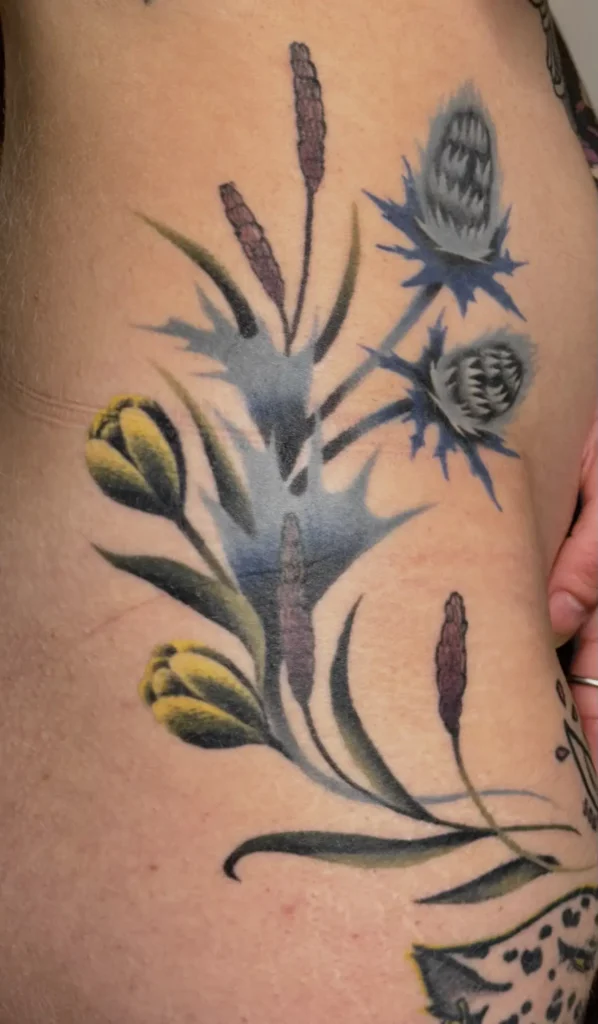 Tatuaje botánico sin línea (lineless) con cardo, lavanda y botón de oro a color, un homenaje familiar realizado por Karratu Tattoo Bilbao
